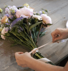 En person binder en bukett med blommor på ett bord.
