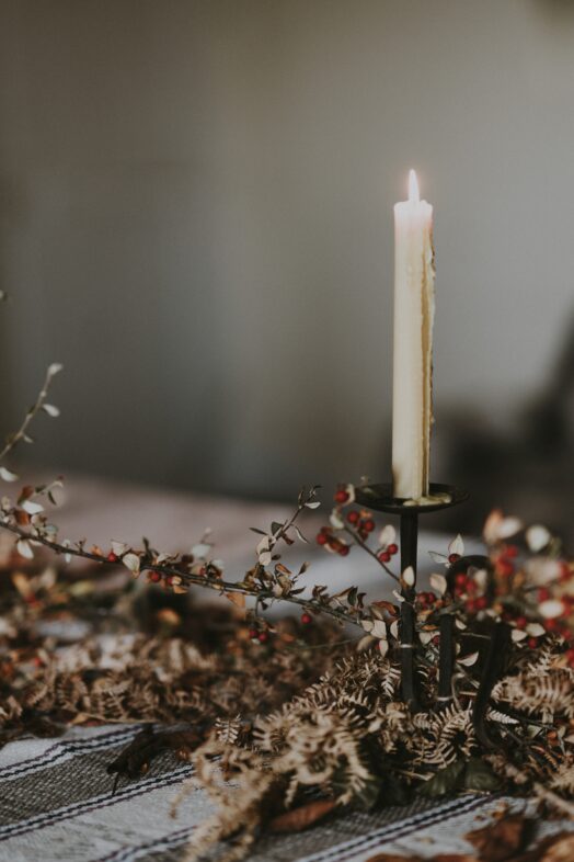 Ett tänt stearinljus står på en bordskiva dekorerad med torkade blommor.