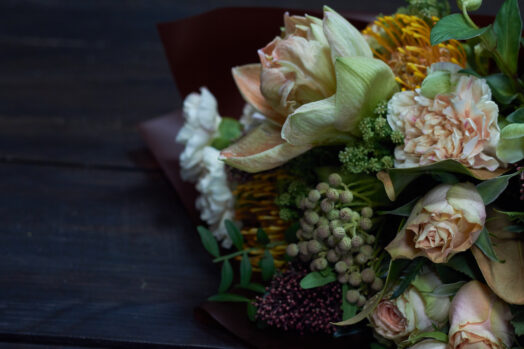 En bukett med ljusa och mörka blommor ligger på ett mörkt bord.